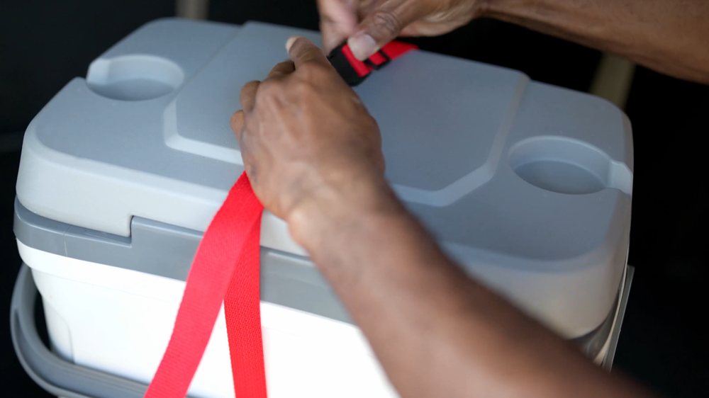 Cooler being fastened securely using a red poly strap and a black plastic buckle. 
